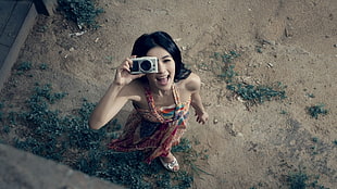 woman wearing halter dress holding gray point-and-shoot camera