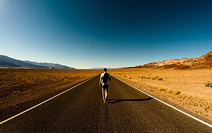 man in white shirt walking on concrete road under blue sky during daytime photo