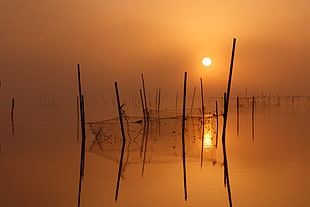 black rods on body of water during sunset