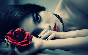 closeup photography of woman laying holding fully bloomed red rose flower