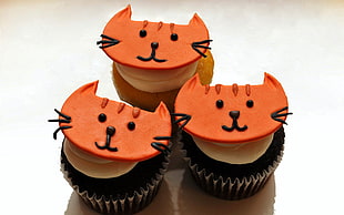 three baked chocolate cupcakes with cat shape decor on top