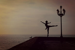 silhouette color of ballerina performing beside street light and ocean at night time