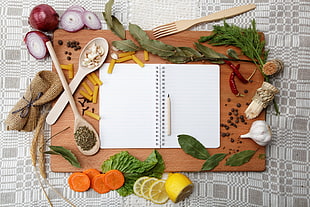 brown wood-frame chopping board with notebook and spices