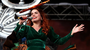 brown-haired woman in green long-sleeved dress holding microphone