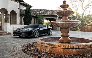 black Ferrari sports coupe parked near outdoor fountain during daytime HD wallpaper