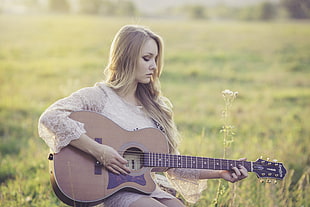 woman playing guitar on grass land during daylight