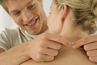 man wearing white shirt putting silver-colored necklace on woman neck