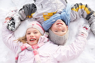 girl and boy in winter jackets smiling while laying