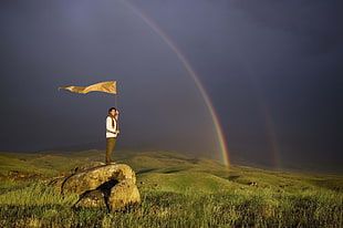 man holding flag standing on rock near grass field