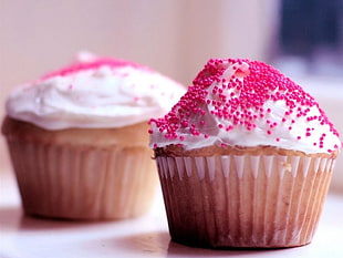 two white cupcakes with pink sprinkles on top