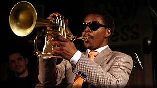 man wearing gray suit jacket playing gold trumpet