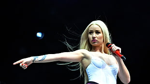 woman wearing white bustier holding red wireless microphone pointing her hand beside photo
