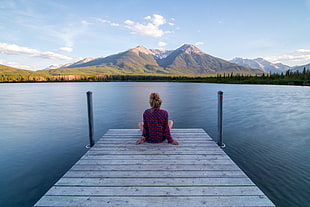 woman in red and blue plaid sports shirt sitting on grey wooden dock bridge under blue and white skies