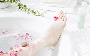 person's feet on white bathtub