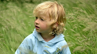 selective focus of blonde hair toddler in teal hoodie surrounded with grass