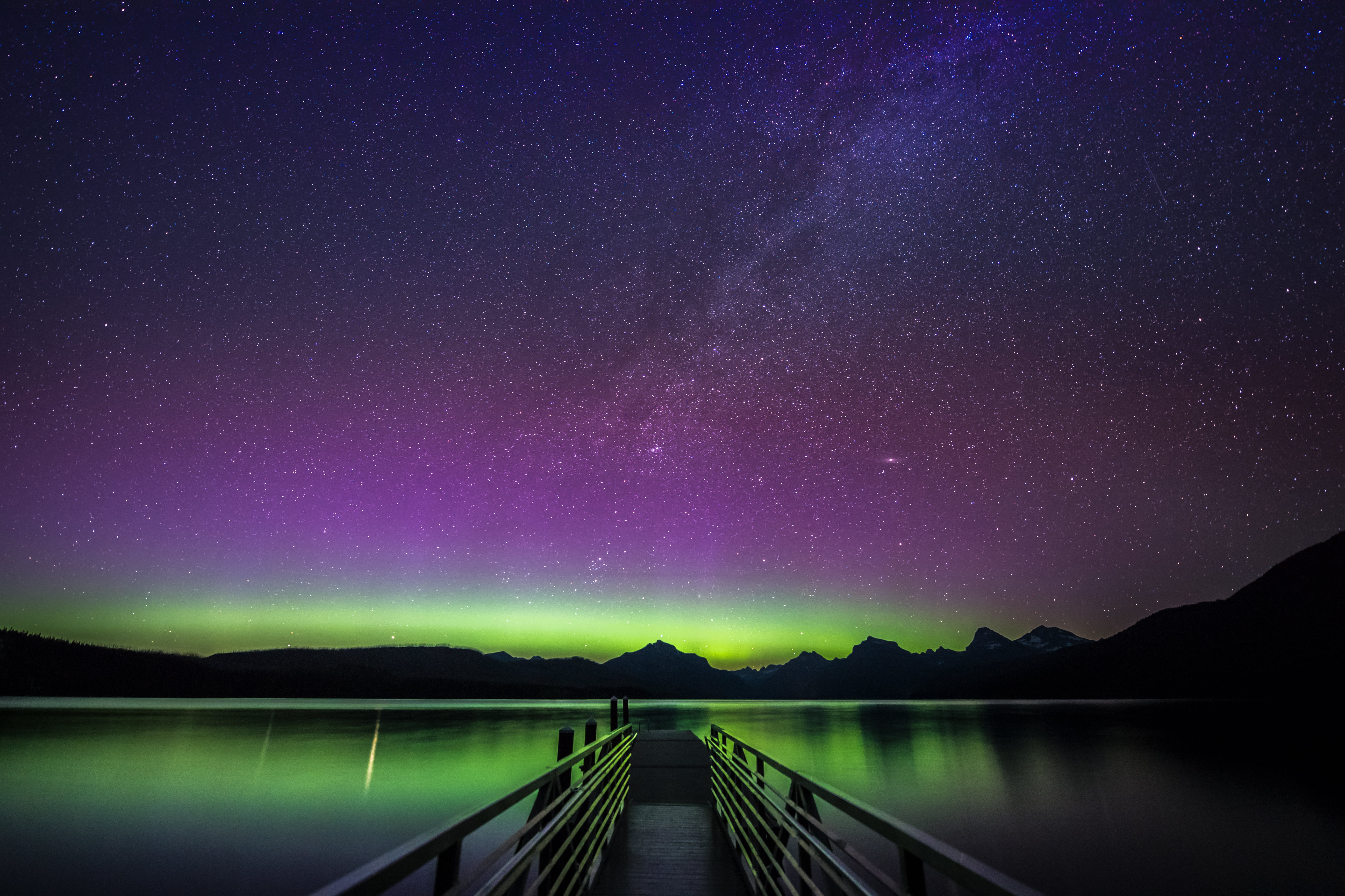 empty dock surrounded with calm body of water under purple and black sky, lake mcdonald, montana