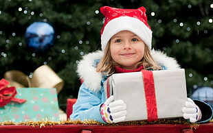 girl in blue jacket with red santa hat holding gift box