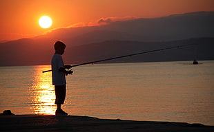 boy holding a fishing rod during sunset