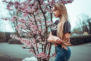 woman in black crew-neck t-shirt and blue denim bottoms standing beside pink flowering tree during daytime