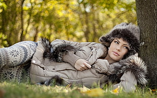 woman wearing gray fur hoodie laying on green grass