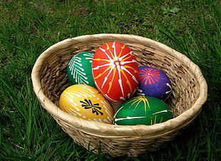 multicolored egg decors in oval brown wicker basket on green grass field