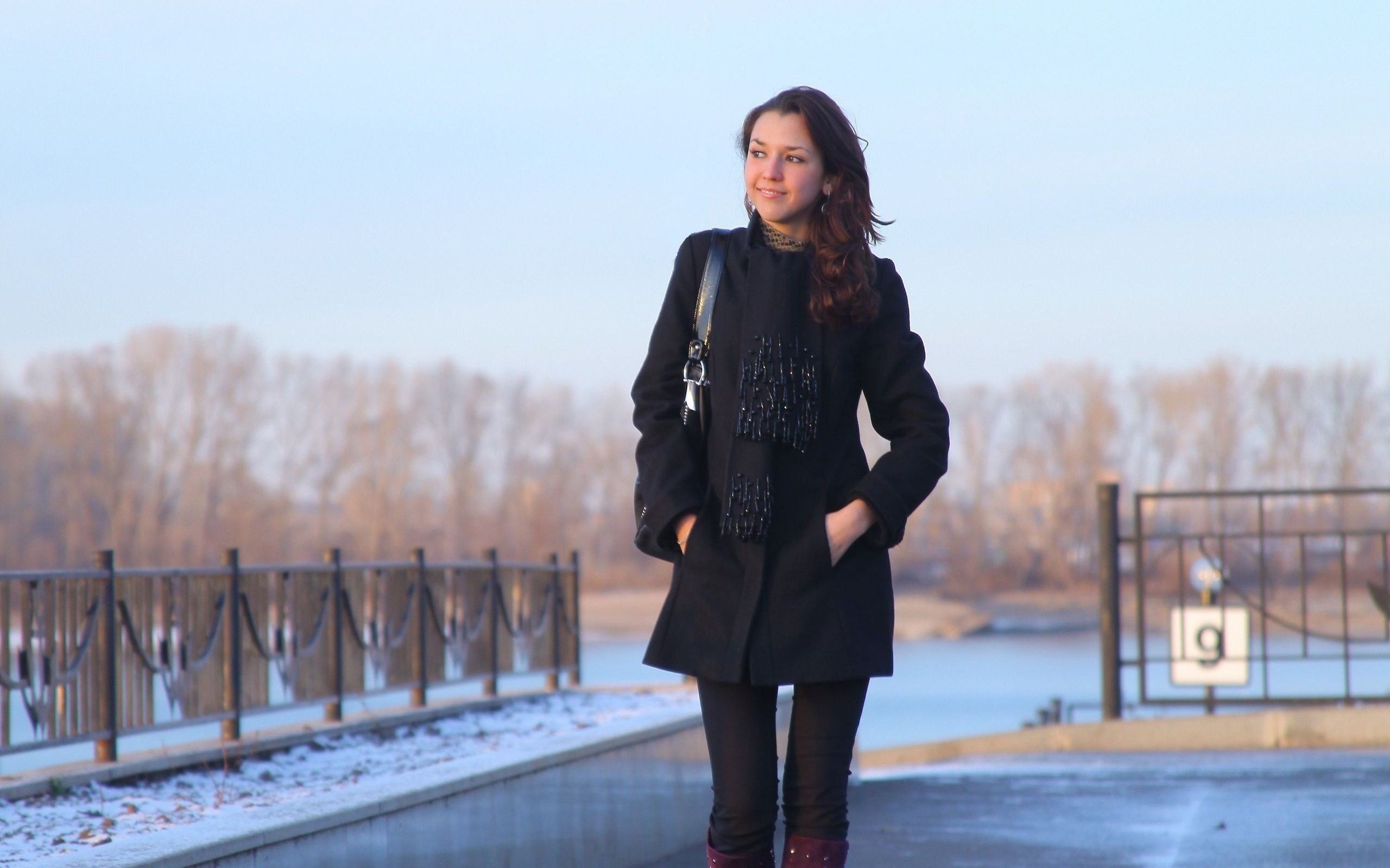 woman wearing black trench coat walking in front of black steel fences