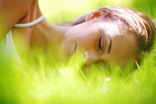 woman in white spaghetti strap top sleeping on clean grass during daytime