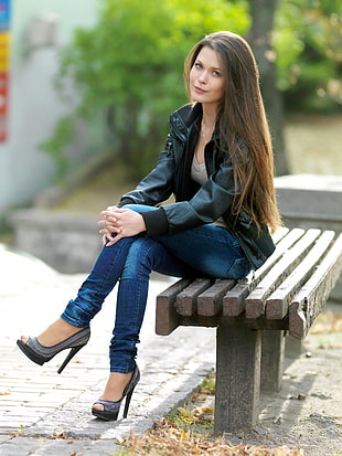 woman wearing black leather full-zip jacket while sitting on gray concrete bench