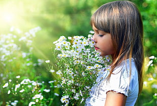 girl smelling white petaled flower photo during daytime