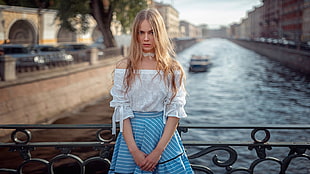 selective focus photography of woman wearing white lace top standing behind the bridge rail