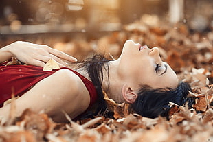 woman in maroon sleeveless dress laying down on a bunch of brown leaves