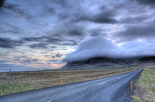 photo of gray road beside green grasses and dark clouds, iceland