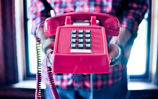 person holding red push-button telephone