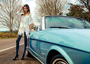 woman wearing white long-sleeved shirt leaning on blue Ford Mustang convertible