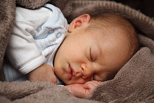 baby in white sleepsuit sleeping on brown fleece textile on focus photo
