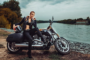 woman wearing black leather jacket with black pants sitting on black touring motorcycle near body of water during daytime