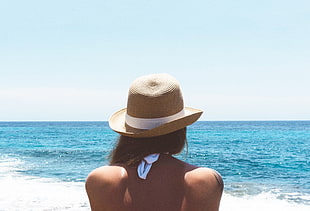 woman with brown bucket hat standing on seashore during daytime