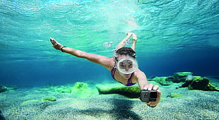 woman swimming underwater holding gray action camera