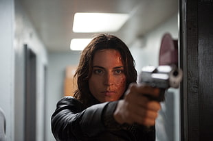 woman wearing black jacket and pointing gun near doors