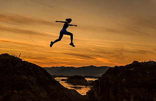 woman jumping on two hill rocks during gold hour