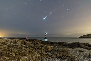 white and black lighthouse in middle of body of water with shooting star, penmon, anglesey