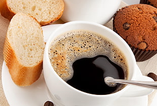 coffee on white ceramic mug beside brown bread