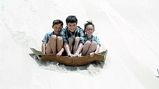 three boys enjoying slide on snow hill