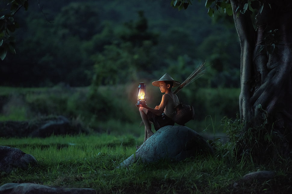 Boy holding black propane lantern sitting on gray rock HD wallpaper