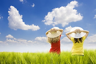 landscape photography of two females on green grass field wearing sun hats