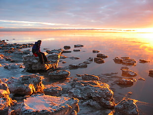 person sitting on a rock near shoreline during golden hour, anchorage, alaska
