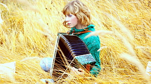 selective focus photography of woman holding accordion on brown grass during daytime