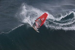 man riding red sail boat surfing
