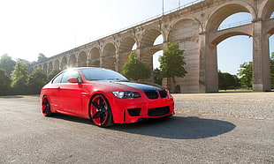 photography of red coupe near brown concrete bridge