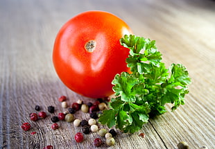 still-life photography of tomato near parsley and peppers on brown wooden surface